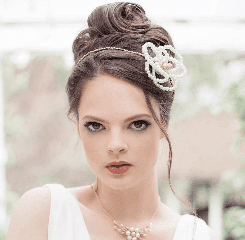 Elegant woman with pearl hair accessory and necklace, wearing a white dress, looking directly ahead.